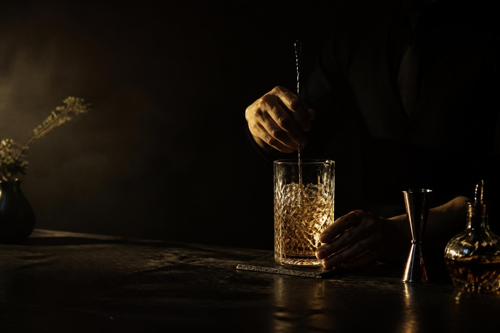Bartender stirring a cocktail in a dark, gold-lit bar